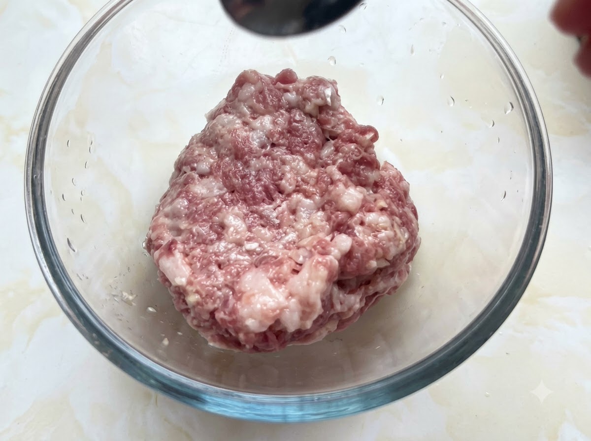 Eine Glasschüssel gefüllt mit Hackfleisch, das von einem Löffel Gewürze erhält.