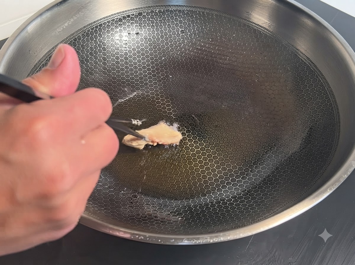 Ein mit Teig umhülltes Hähnchenstück wird mit Stäbchen in einen heißen Metallwok mit Öl gegeben.