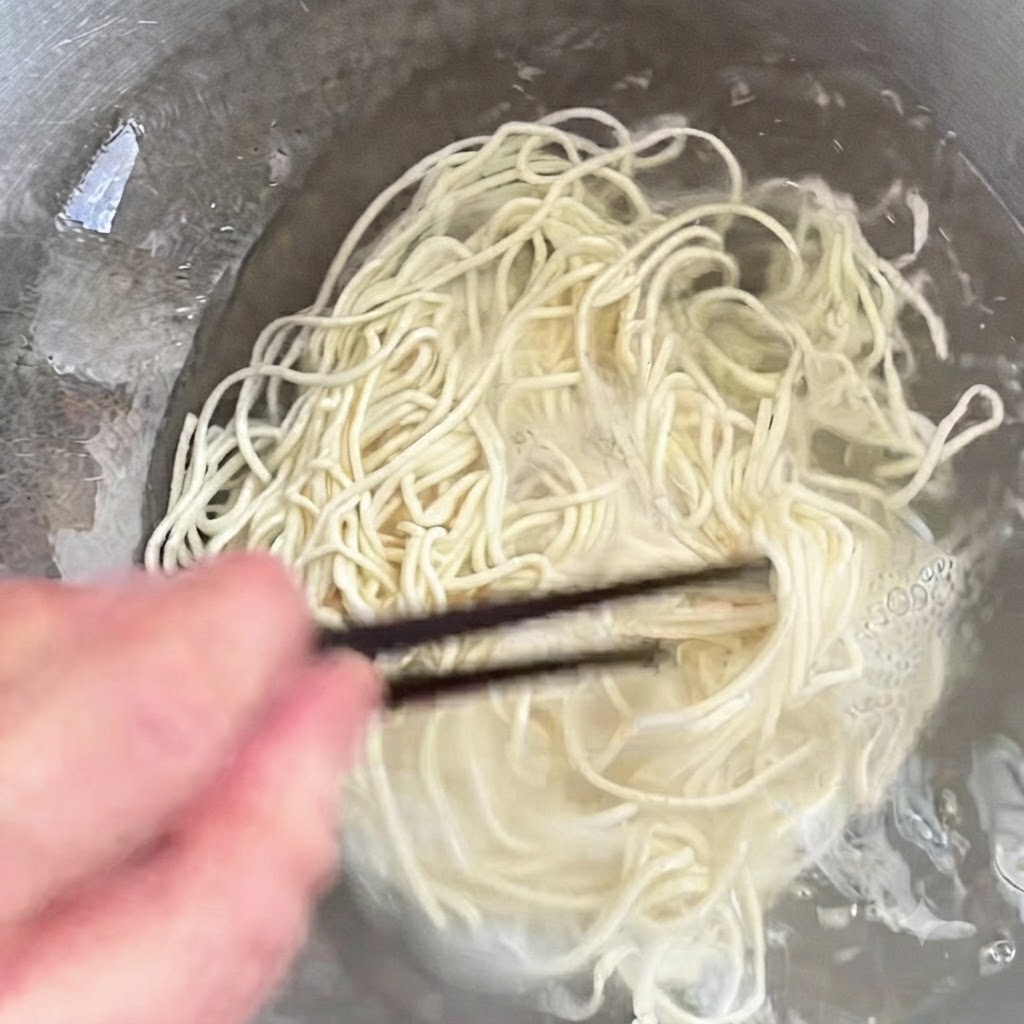 Nudeln kochen in einem Topf und werden mit Stäbchen umgerührt.