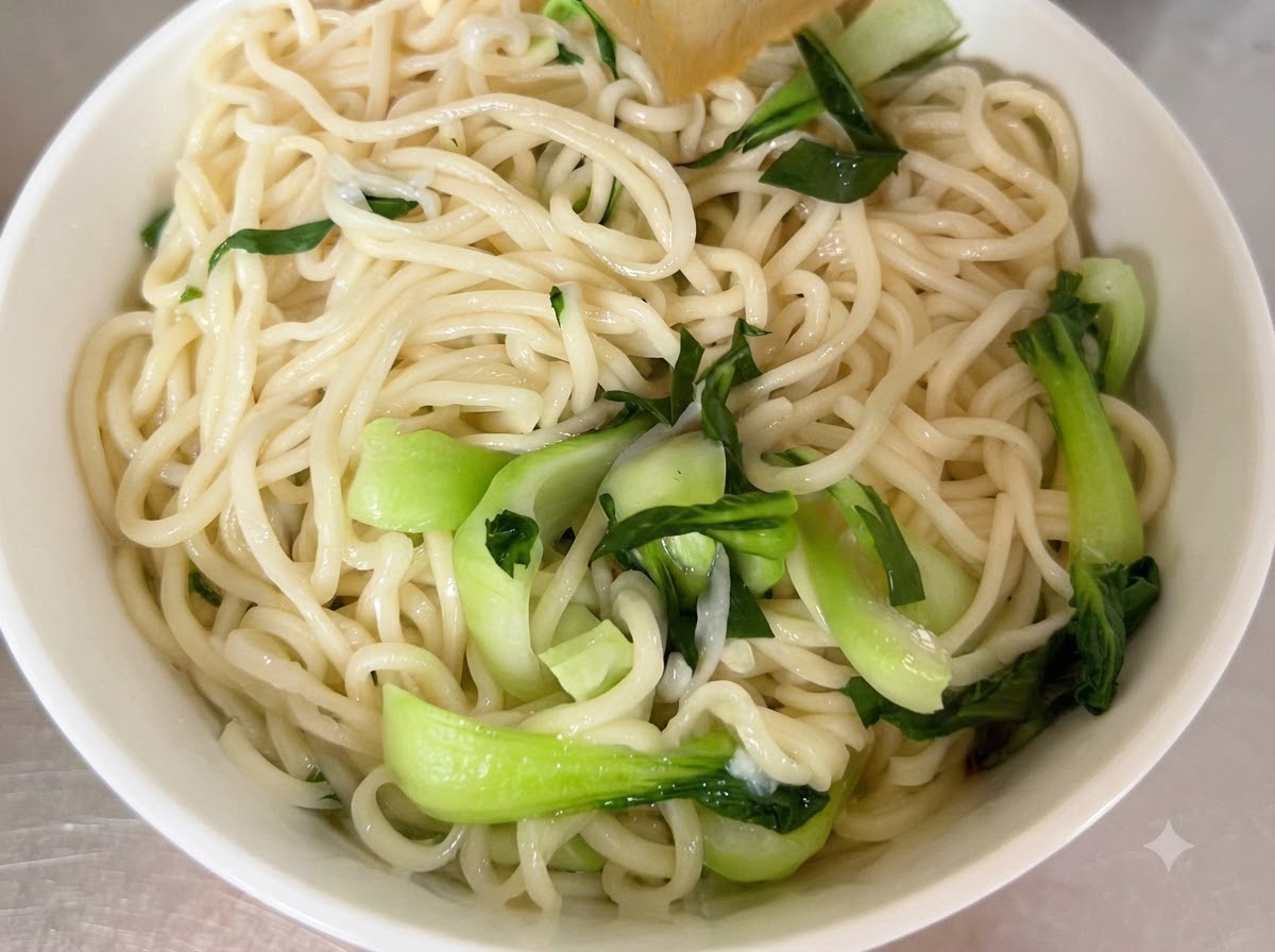 Gekochte Nudeln und frischer Pak Choi in einer weißen Servierschüssel angerichtet.