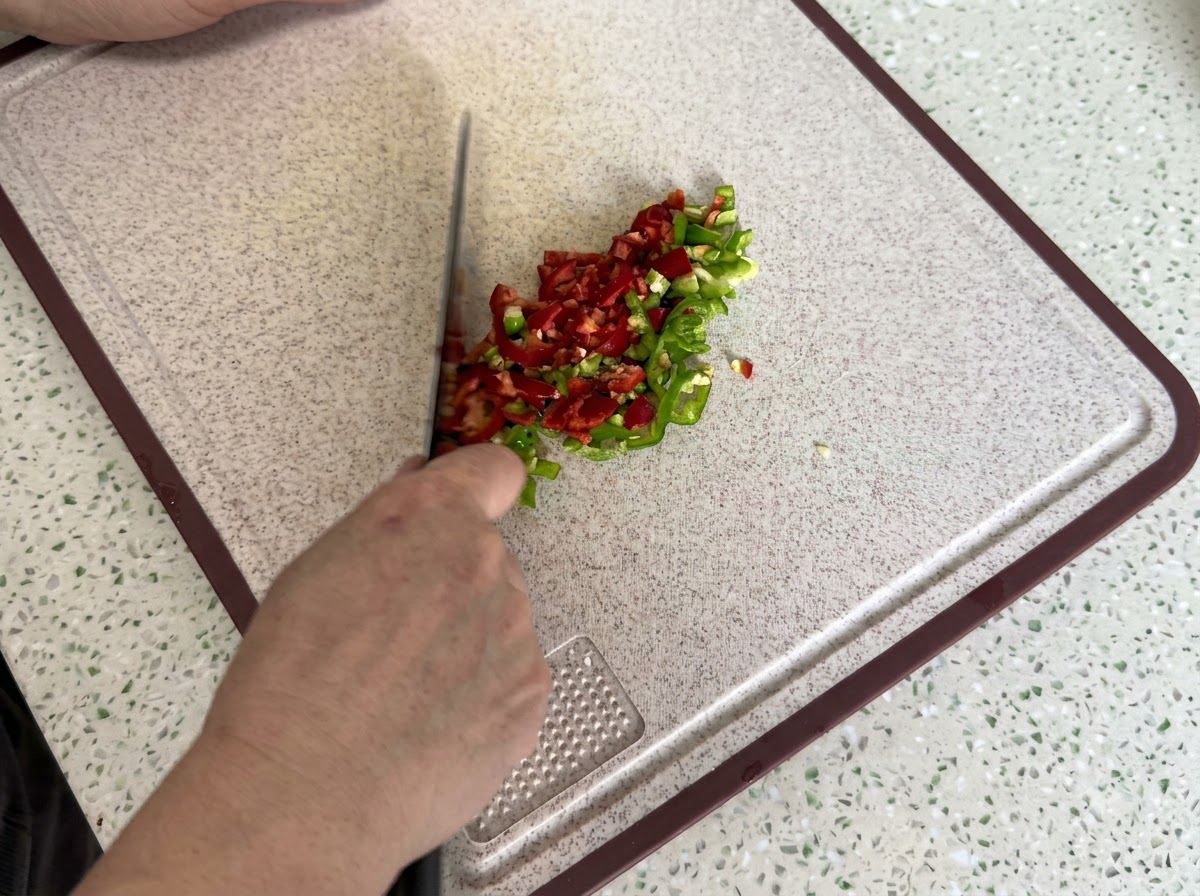 Rote und grüne Chilischoten fein geschnitten und gewürfelt auf einem sauberen Schneidebrett.