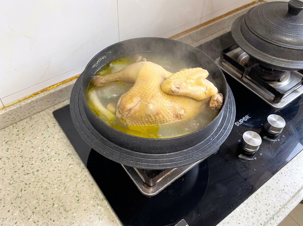 Ein gekochtes ganzes Hähnchen köchelt in einem Topf, bevor es in Stücke portioniert wird.