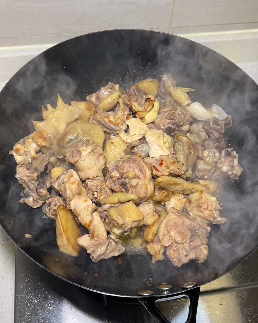 Goldgelb angebratene Hähnchenstücke werden in einem Wok mit aufsteigendem Dampf gekocht.