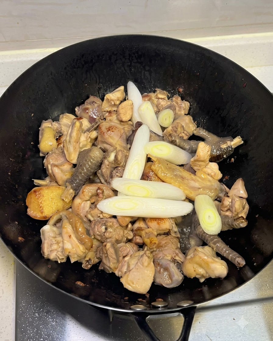 Frühlingszwiebeln, Knoblauch und ganze Gewürze werden in den Wok zum Hähnchen gegeben.