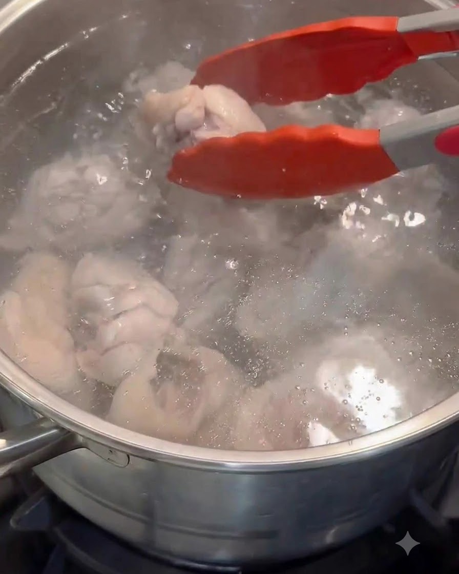 Rote Zangen geben blanchierte Hähnchenstücke in einen Topf mit frischem, heißem Wasser.