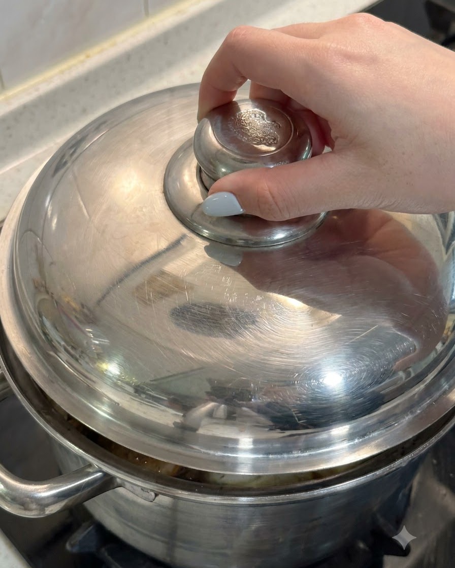 Eine Hand legt den Metalldeckel auf einen Topf voller Hähnchen und Suppenzutaten.