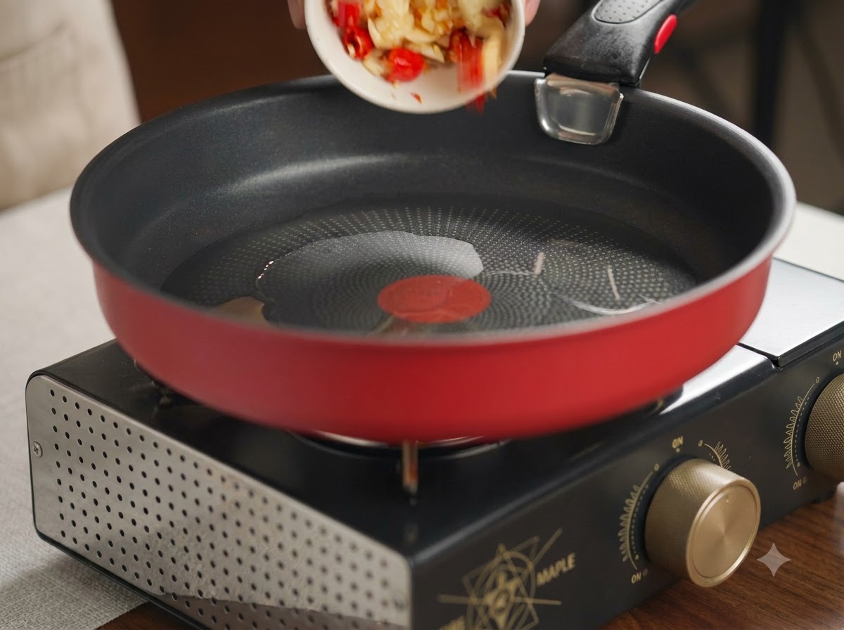 Zerstoßener Knoblauch und rote Chilis werden aus einer kleinen weißen Schale in eine heiße rote Pfanne mit Öl gegeben.