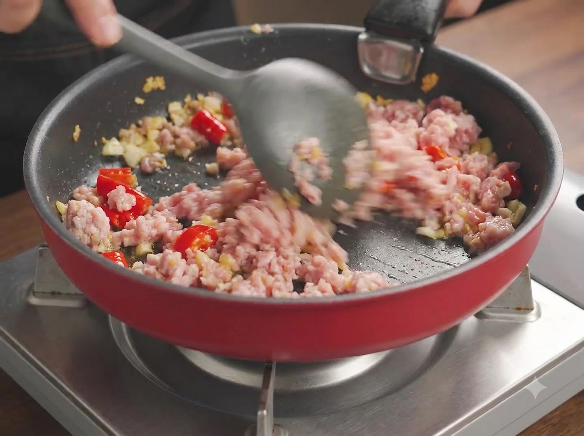 Schweinehackfleisch wird in einer Pfanne kräftig zerkleinert und mit Chilis und Knoblauch angebraten.