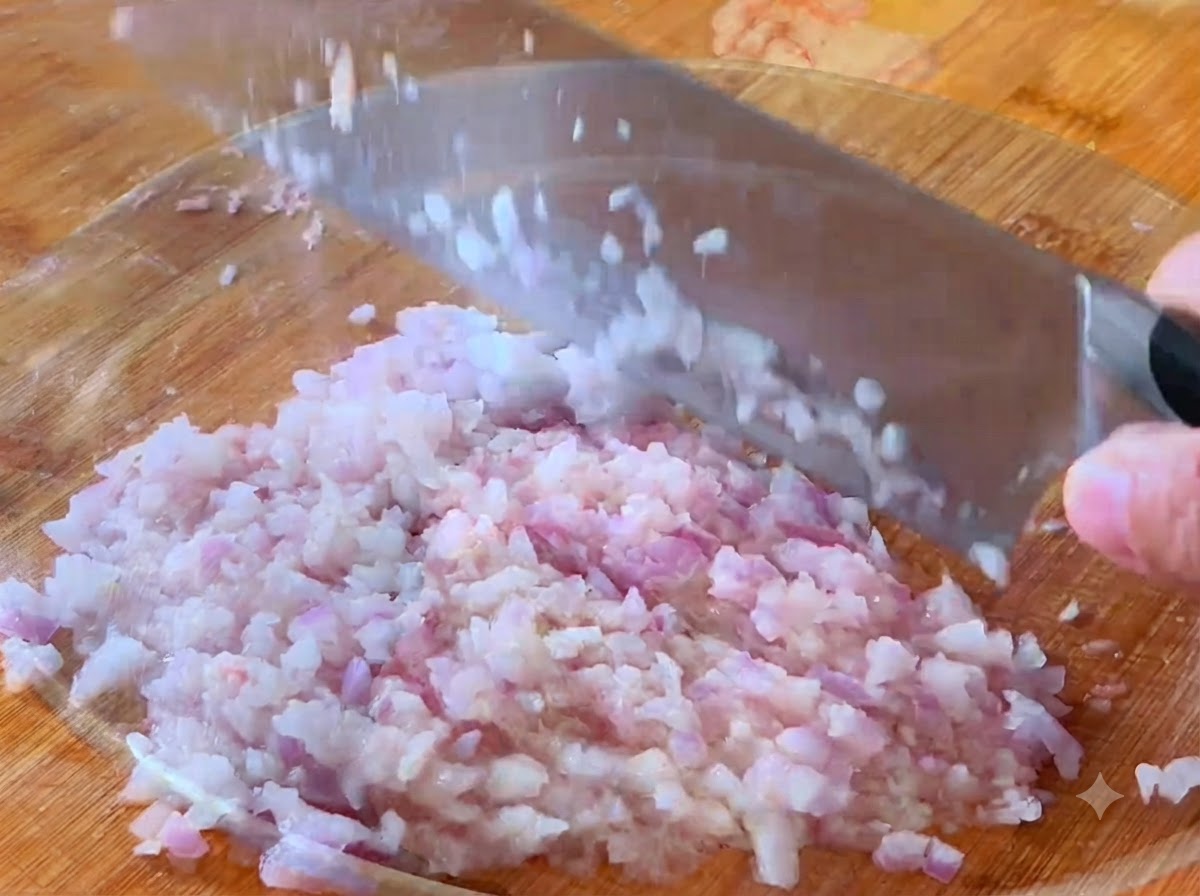 Eine Zwiebel wird mit einem Küchenmesser auf einem Schneidebrett in kleine Stücke gewürfelt.