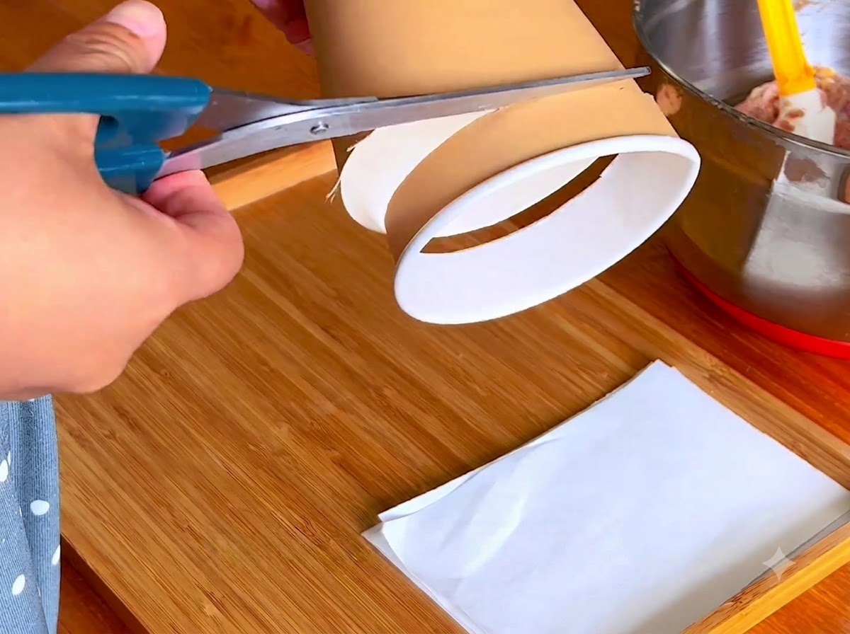 Eine Schere schneidet den unteren Rand eines Papierbechers auf einem Holzbrett ab.