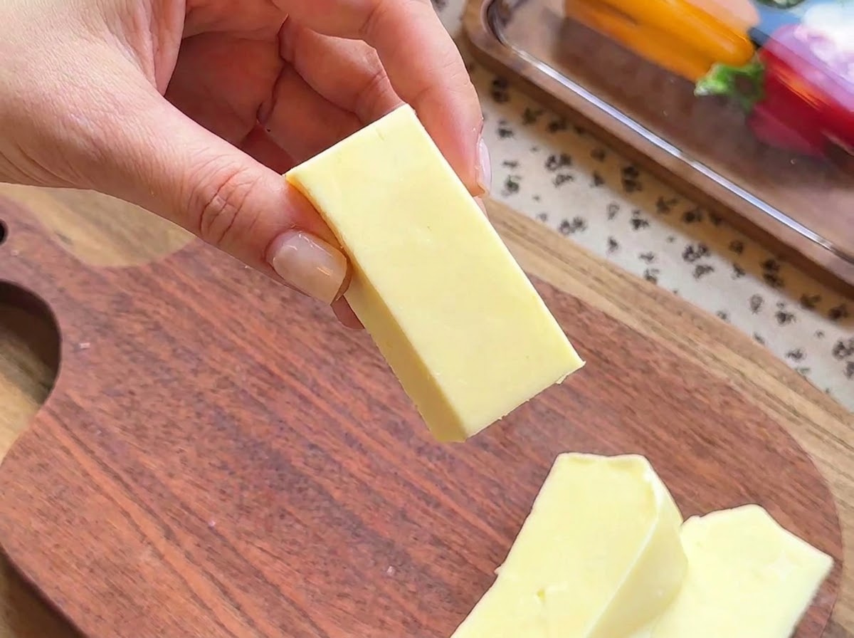 Nahaufnahme einer Hand, die einen rechteckigen Block Mozzarellakäse hält, der zum Füllen vorbereitet wird.