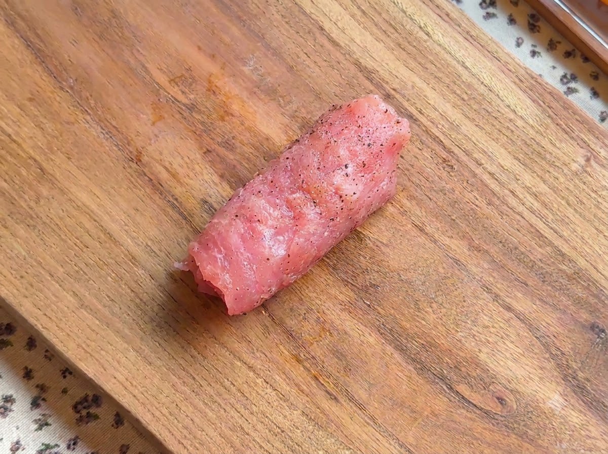 Eine gerollte Stück gewürztes Schnitzel liegt auf einem Holzbrett.