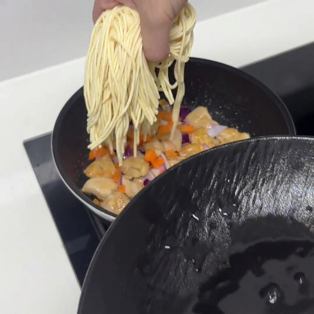 Vorgeweichte Nudeln werden in die Pfanne mit Hähnchen und Gemüse gegeben.