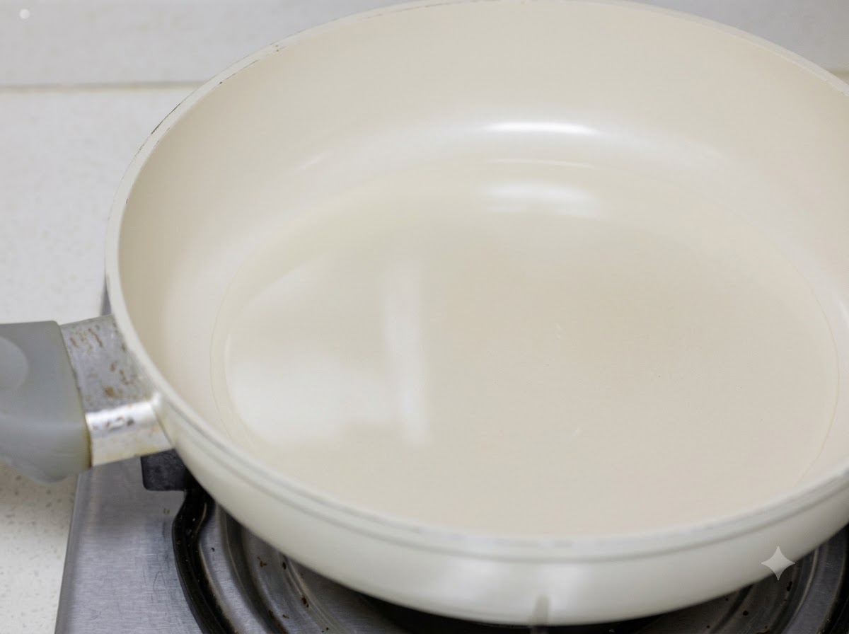 Hähnchenstücke werden in Speiseöl in einer weißen Pfanne angebraten.