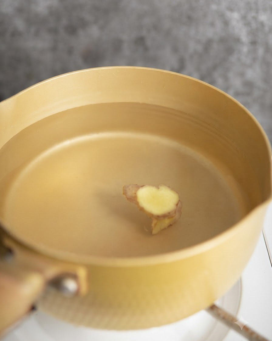 Hähnchenstücke werden in einem Topf mit Wasser und Ingwerscheiben blanchiert.