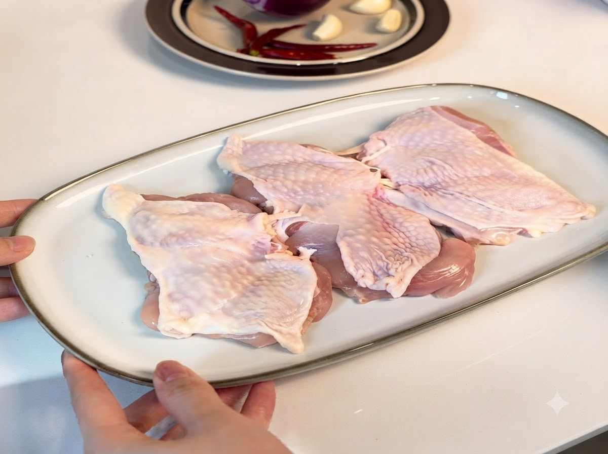 Knochenlose Hähnchenschenkel auf einem weißen Servierteller angeordnet, mit Gewürzen bestreut.