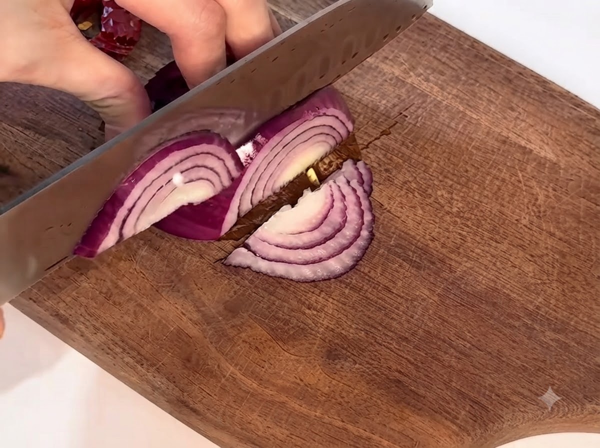 Eine rote Zwiebel wird vorsichtig auf einem Holzschneidebrett mit einem Messer geschnitten.