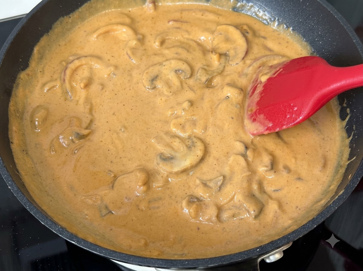 Pilzscheiben gemischt in einer köchelnden Curry-Creme-Soße in einer Pfanne.