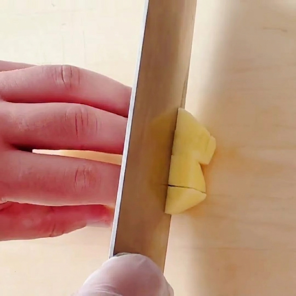 Kartoffeln werden auf einem Holzschneidebrett in kleine quadratische Würfel geschnitten.