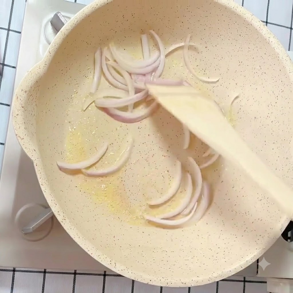 In Scheiben geschnittene weiße und violette Zwiebelstreifen werden in einer bebutterten Pfanne mit einem Holzspatel angebraten.