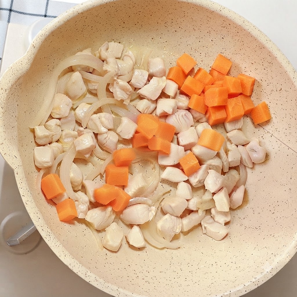 Leuchtend orangefarbene Karottenwürfel werden in die Pfanne mit Hähnchen und Zwiebeln gegeben.