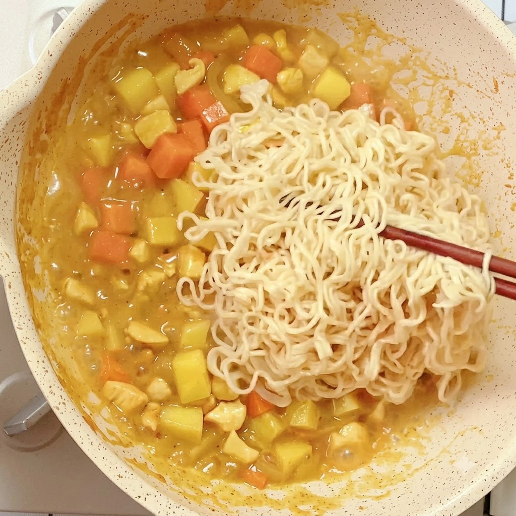 Vorgekochte Instant-Nudeln werden mit Stäbchen in eine Pfanne mit reduzierender Curry-Mischung gegeben.