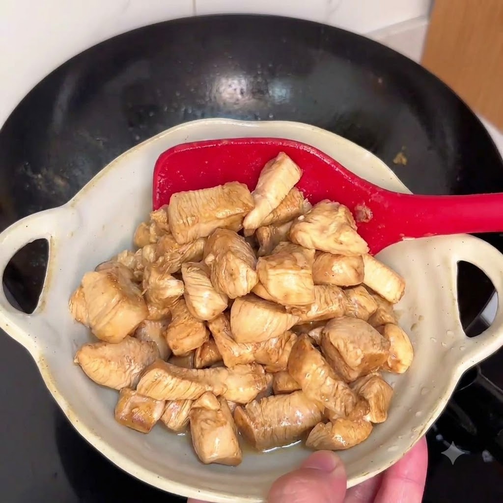 Hähnchenstücke, die in einem heißen Wok mit einem roten Pfannenwender angebraten werden.