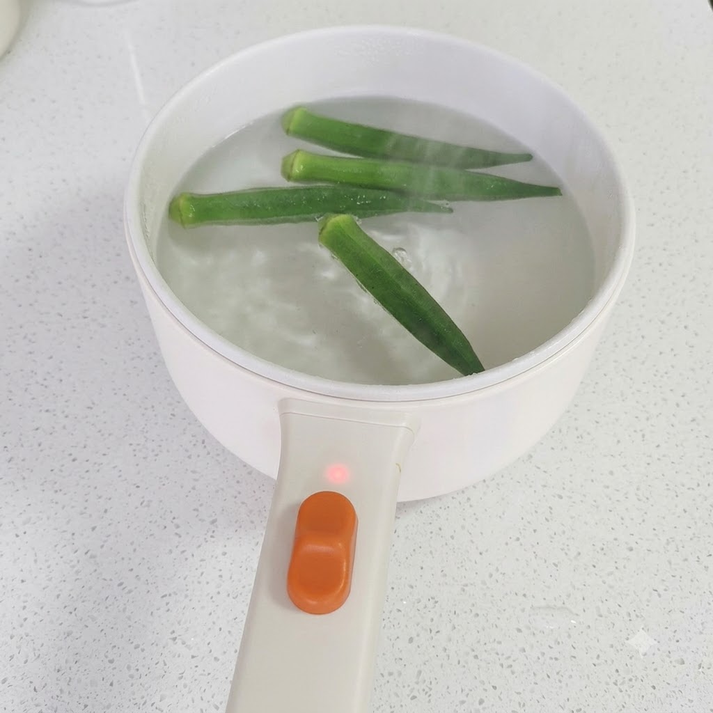 Stäbchen heben gekochten grünen Okra aus einem Topf mit siedendem Wasser.