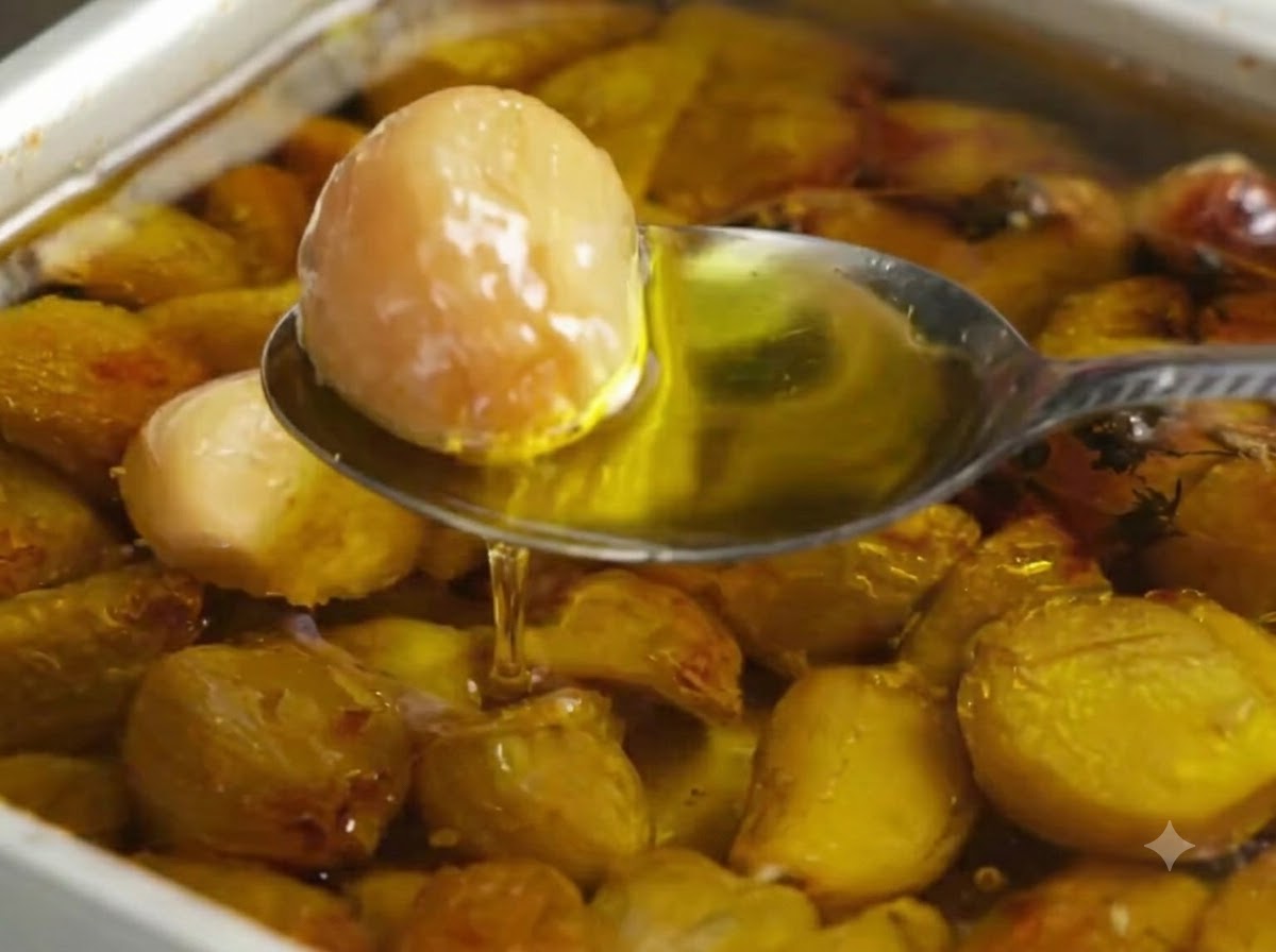 Ein Löffel schöpft eine goldene, geröstete Knoblauchzehe aus einer mit Olivenöl und Knoblauch gefüllten Backform.