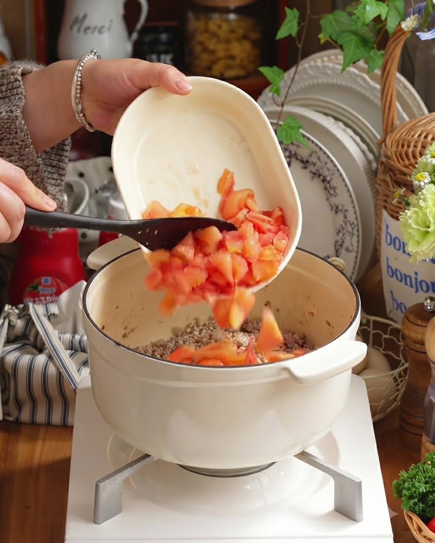 Geschälte gewürfelte Tomaten und gehacktes Gemüse werden in den Topf zum Fleisch gegeben.