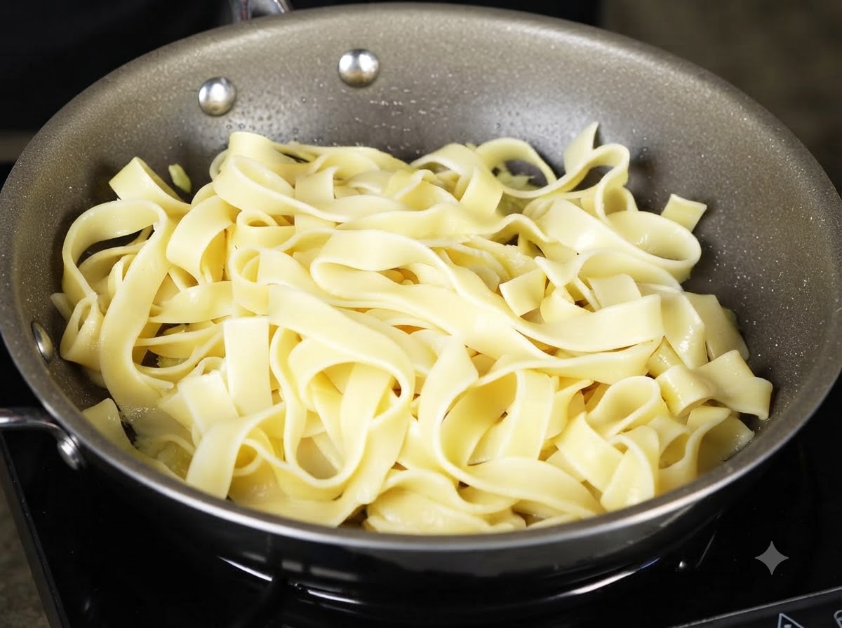 Eine Schöpfkelle giesst stärkehaltiges Pastawasser über die Nudeln in der Kochpfanne.