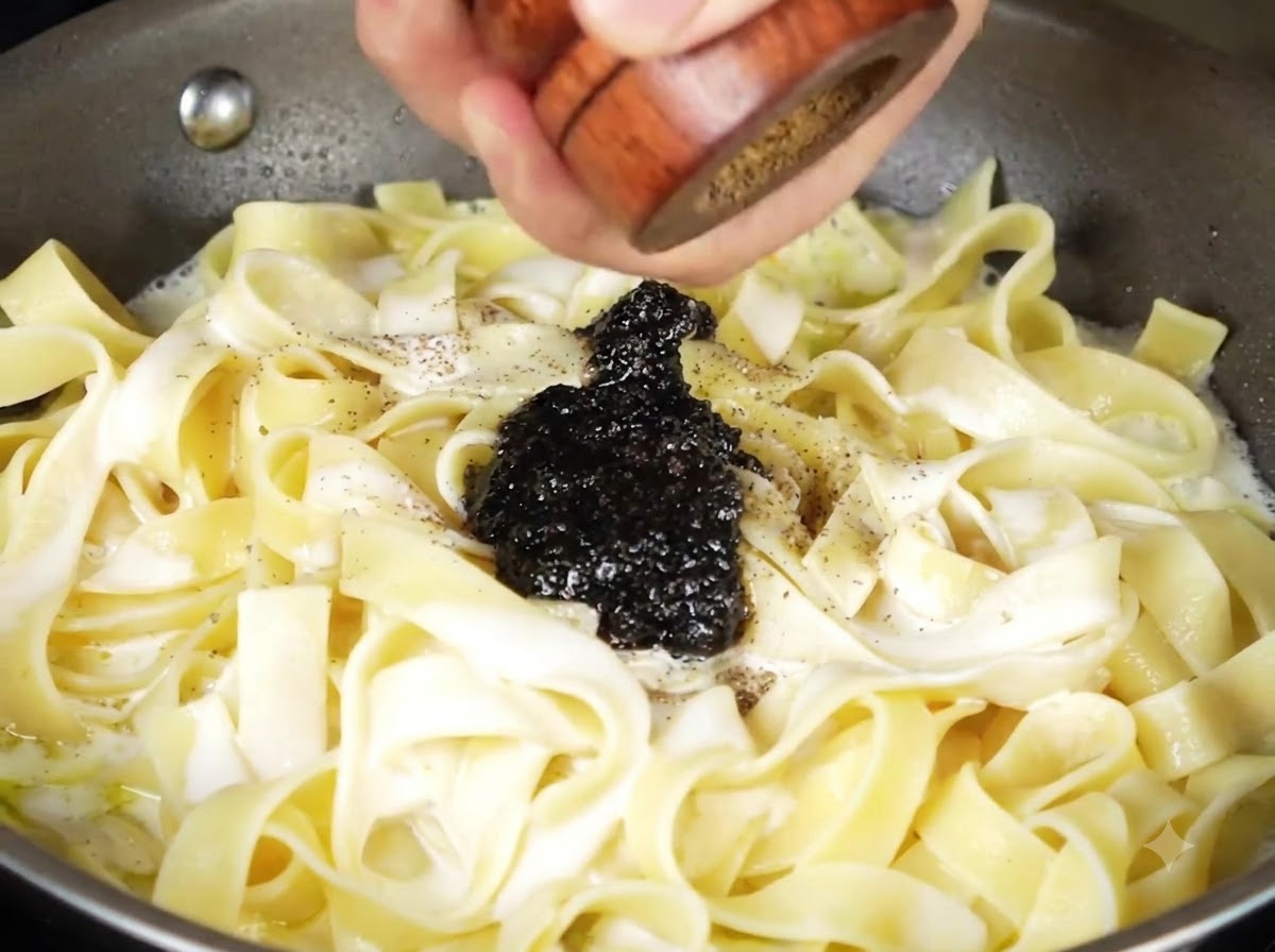 Schwarze Trüffelsauce und frisch gemahlener schwarzer Pfeffer auf der cremigen Pasta in der Pfanne.