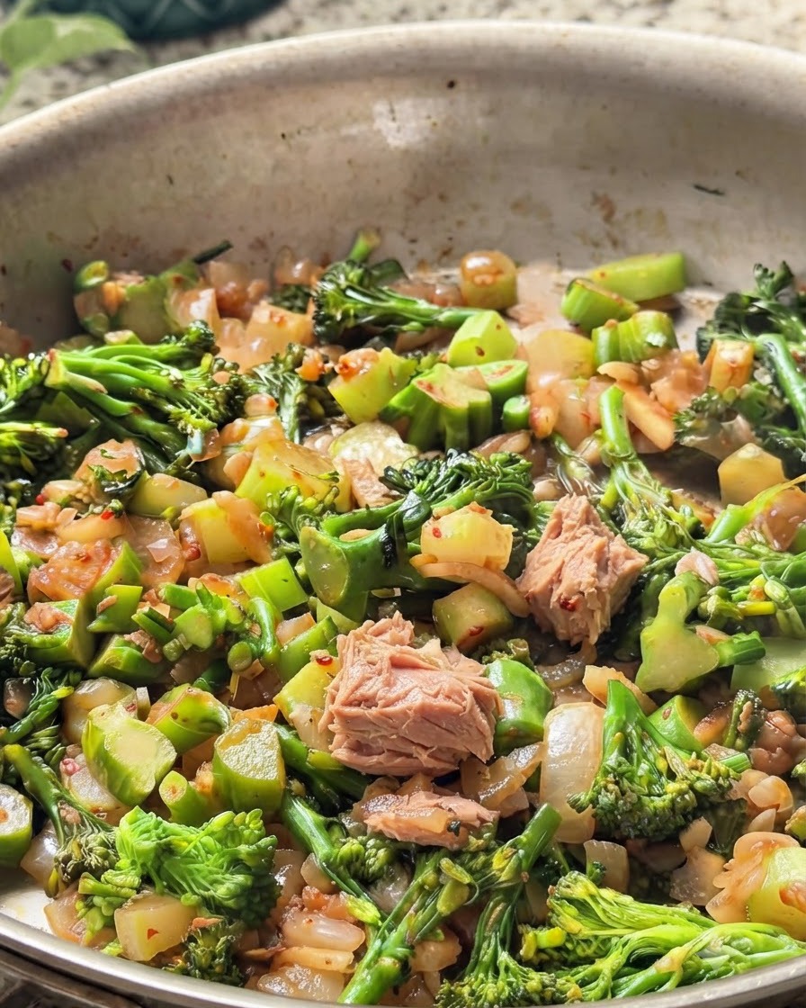 Stücke von Dosenthunfisch in der Pfanne vermischt mit grünem Brokkoli und Zwiebeln.
