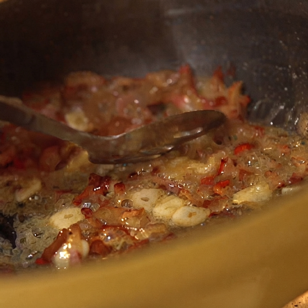 Dosen-Tomatenstücke werden mit einem Löffel in die brutzelnden Pfannenzutaten eingearbeitet.