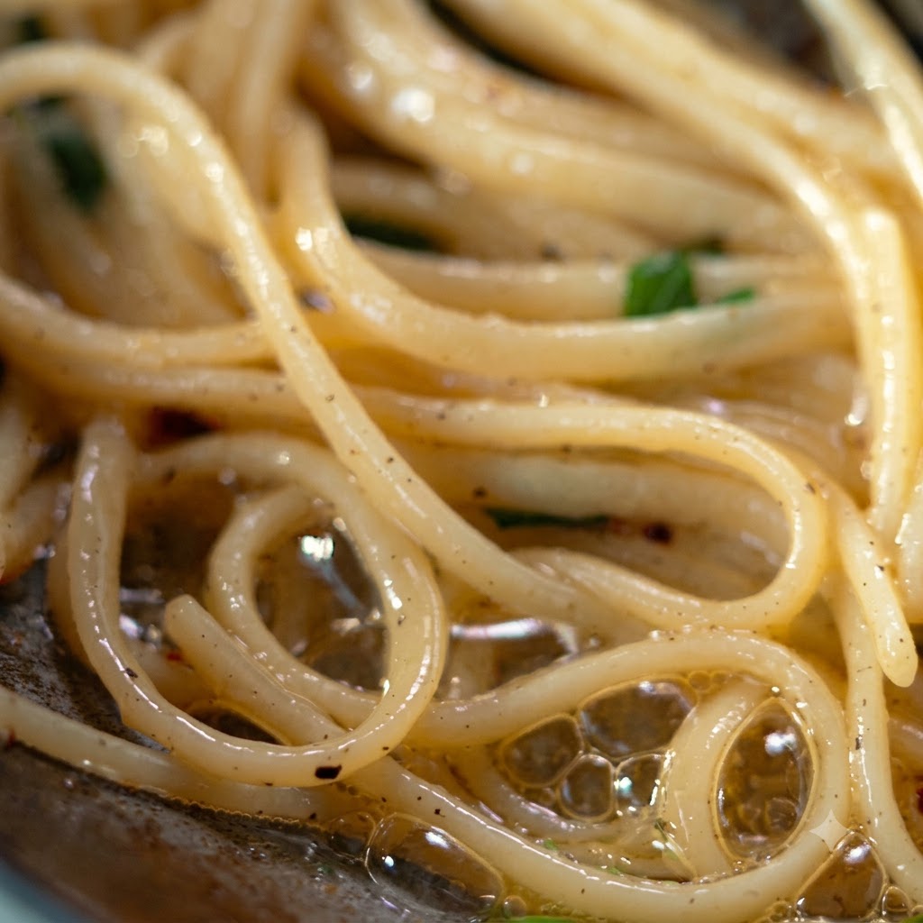 Eine Schöpfkelle und eine Zange heben und übertragen gewürzte Pasta auf einen silbernen Teller.
