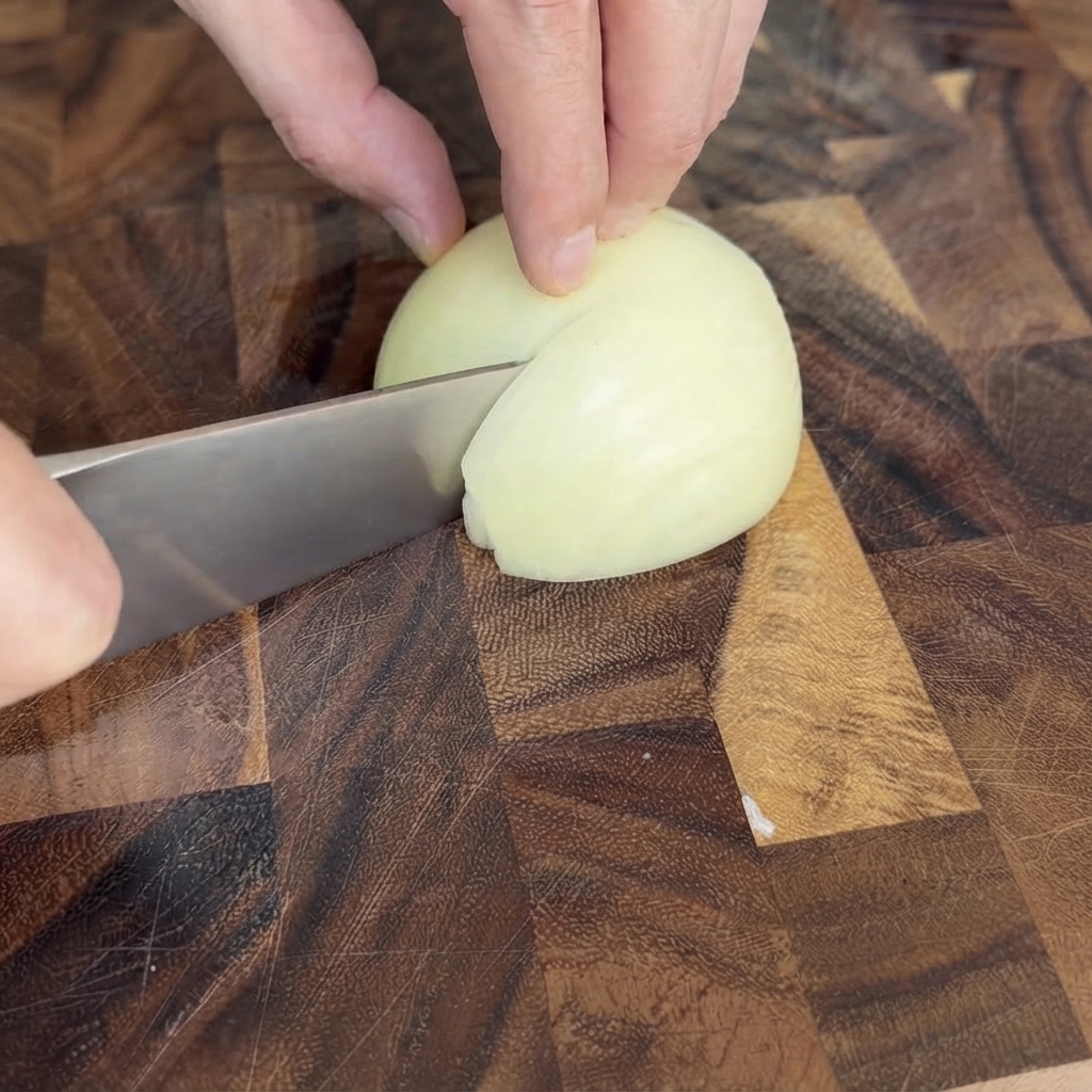 Eine halbe weiße Zwiebel wird auf einem Holzschneidebrett fein gewürfelt.