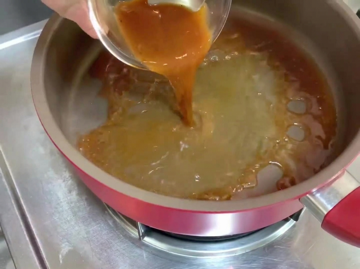 Schwarze Pfeffersoße wird in eine heiße Pfanne gegossen und bildet blubbernde Flüssigkeit.