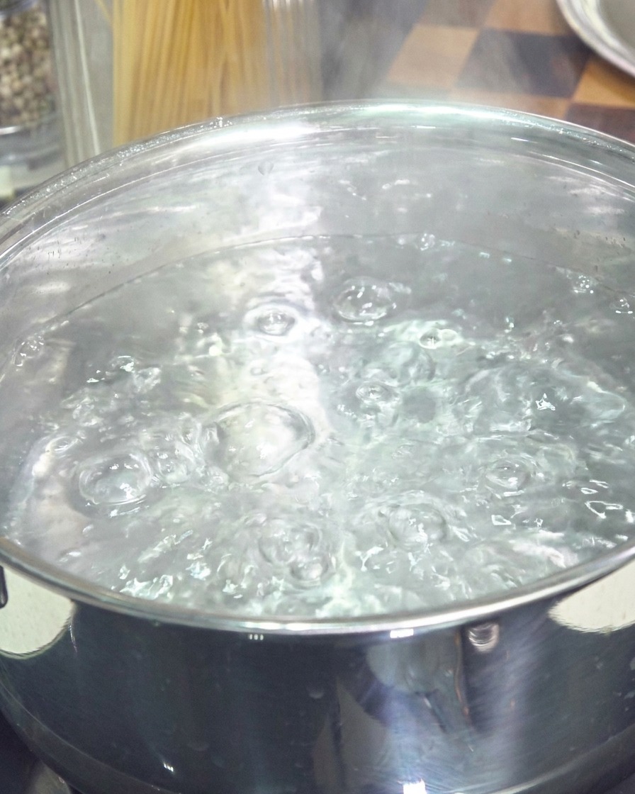 Ein Edelstahltopf gefüllt mit kräftig kochendem Wasser und Blasen, die an die Oberfläche steigen.