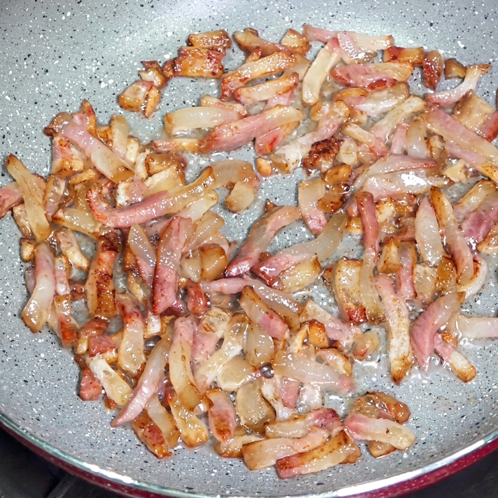 Guanciale-Streifen braten in einer Pfanne, gebenklares Fett frei und entwickeln knusprige, gebräunte Ränder.