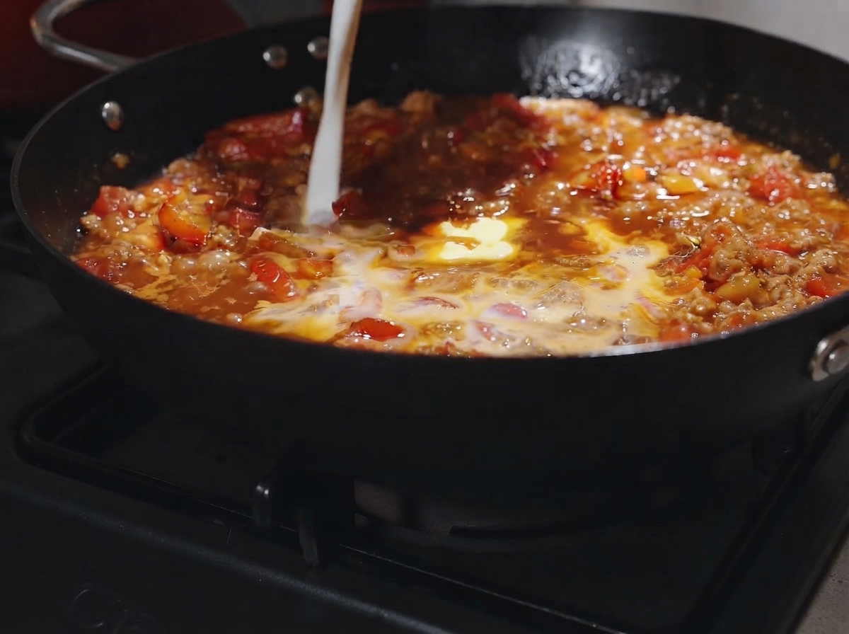 Ein Stück Butter und ein Schlitzer Milch werden in die blubbernde Tomaten-Fleisch-Sauce gegossen.