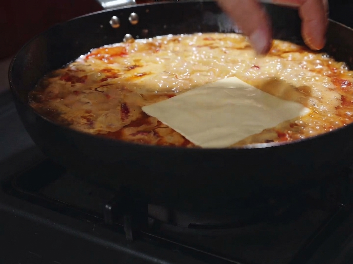 Eine Käsescheibe liegt flach über der blubbernden cremigen Sauce in der Pfanne.