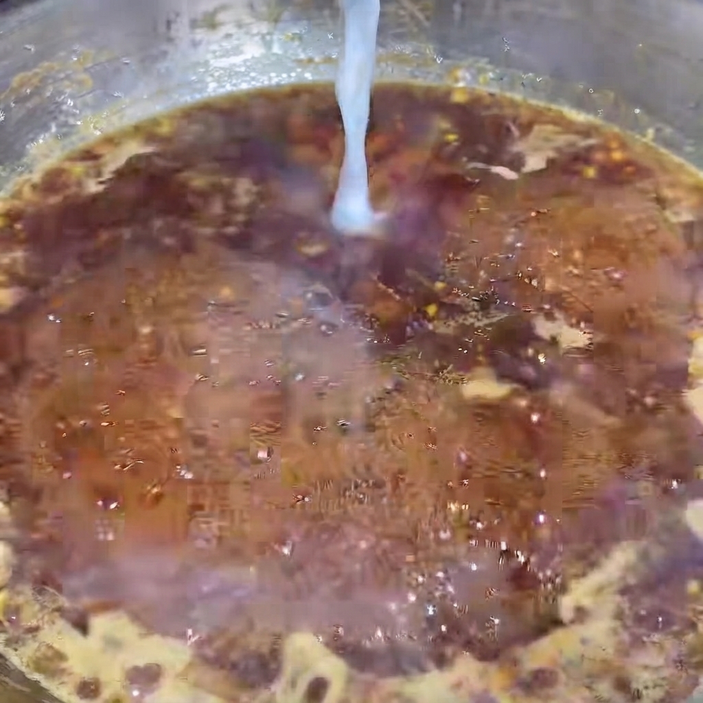 Ein dünner Strahl weißes Stärkewasser wird in eine sprudelnde, dunkle Pfeffersauce in einer heißen Pfanne gegossen.