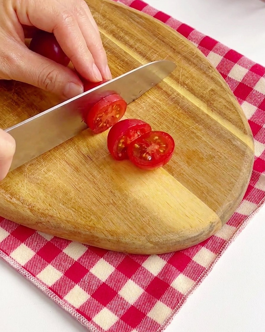 Hände halbieren leuchtend rote Kirschtomaten auf einem Holzschneidebrett.