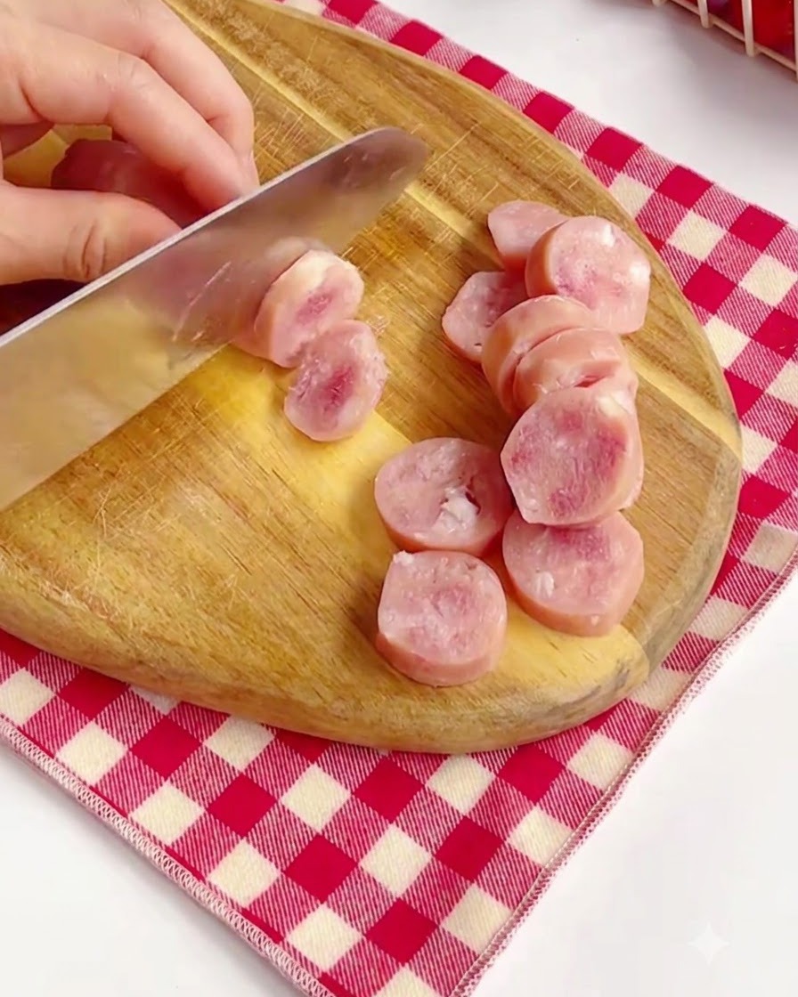 Rosafarbene Würstchen werden auf einem Holzbrett in runde Scheiben geschnitten.