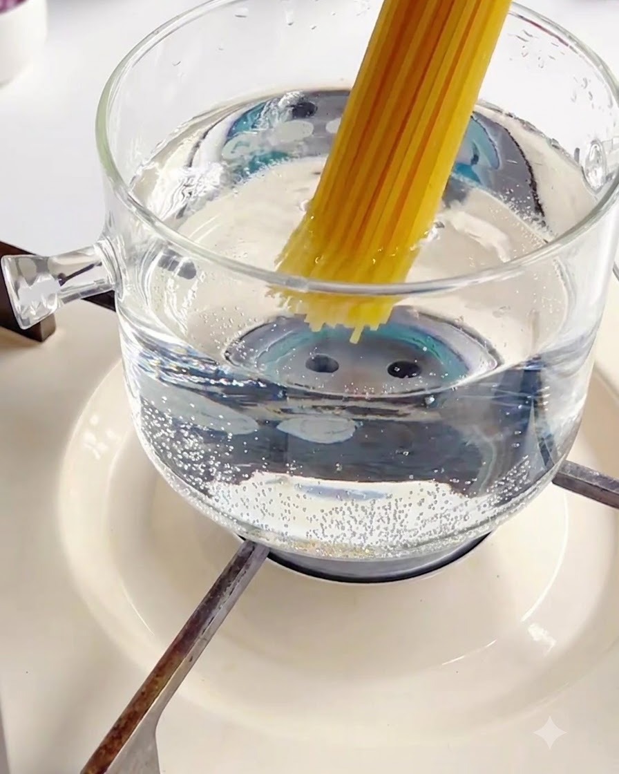 Ein Bündel trockener Spaghetti wird in einen sprudelnden Glastopf mit heißem Wasser gegeben.