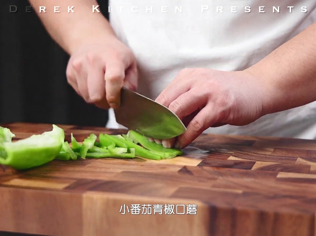Grüne Paprika wird auf einem Holzschneidebrett in feine Streifen geschnitten.