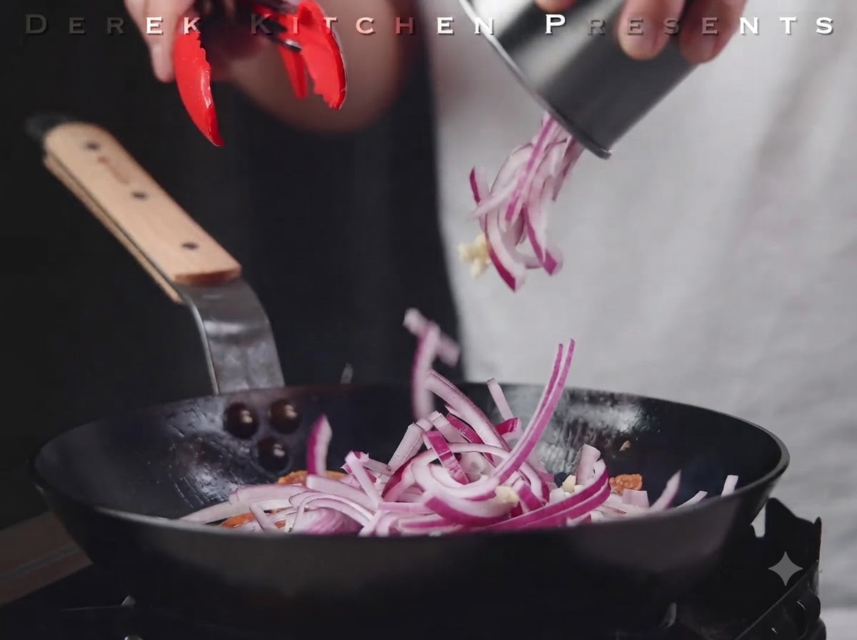 Geschnittene rote Zwiebeln und Knoblauch werden über die Salami in die Pfanne gegeben.