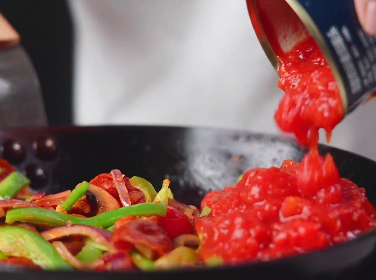 Gehackte Dosentomaten werden in die Pfanne zu Gemüse und Salami gegossen.