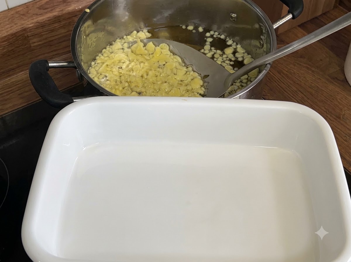 Ein Schaumlöffel schöpft blassgelbe frittierte Tempura-Flocken aus einem Öltopf in ein weißes Tablett.