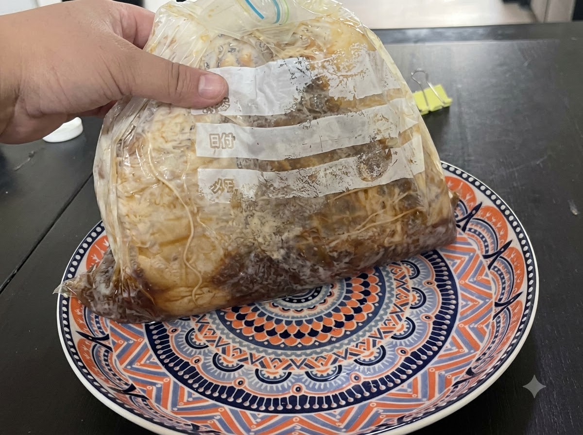 Eine Hand hält einen vakuumversiegelten Beutel mit mariniertem Fleisch auf einem gemusterten Teller.